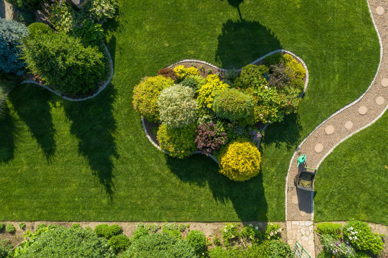 Aerial view of a manicured lawn with planted beds and a stone walkway by Your Company Name